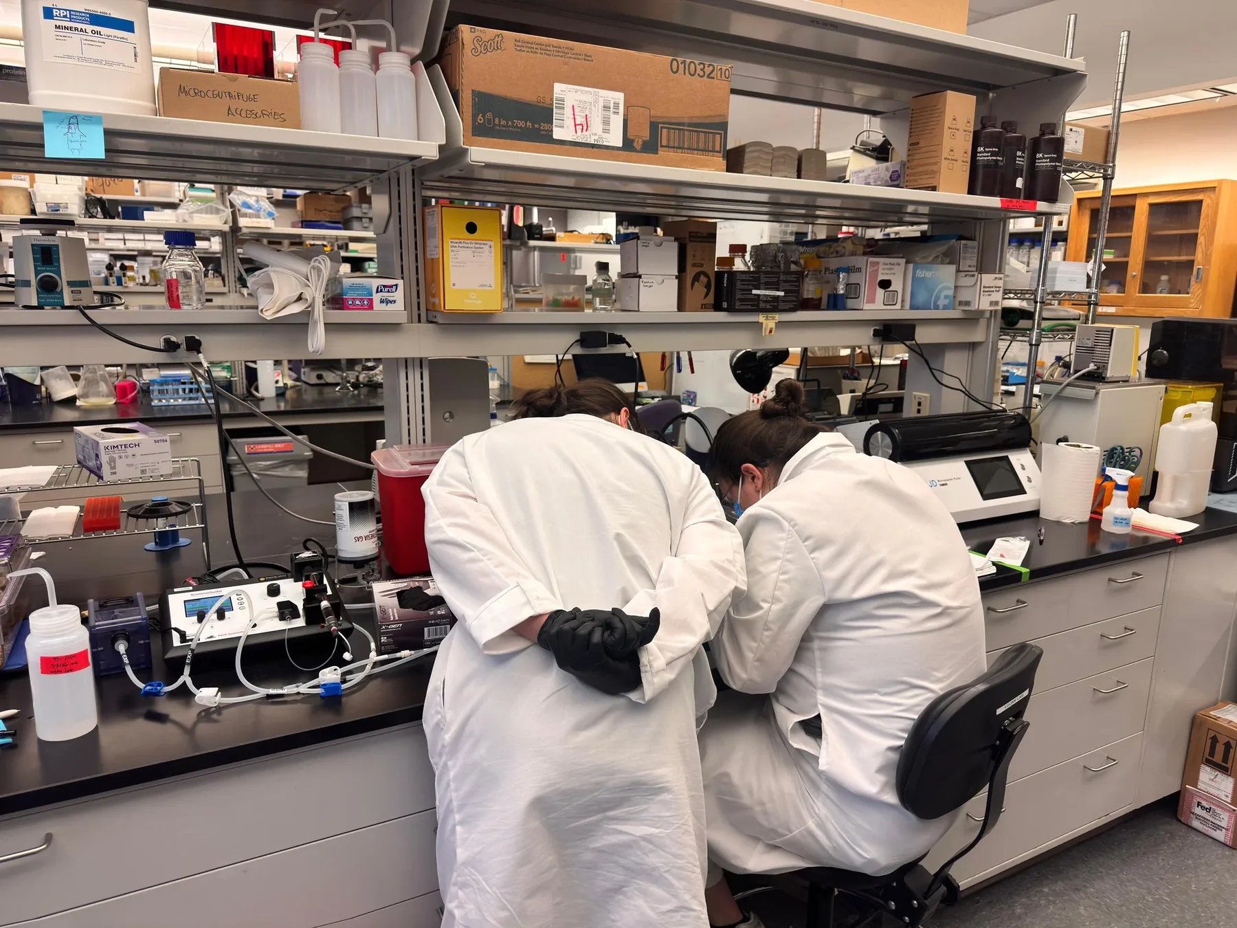 Two lab members in lab coats working at the bench