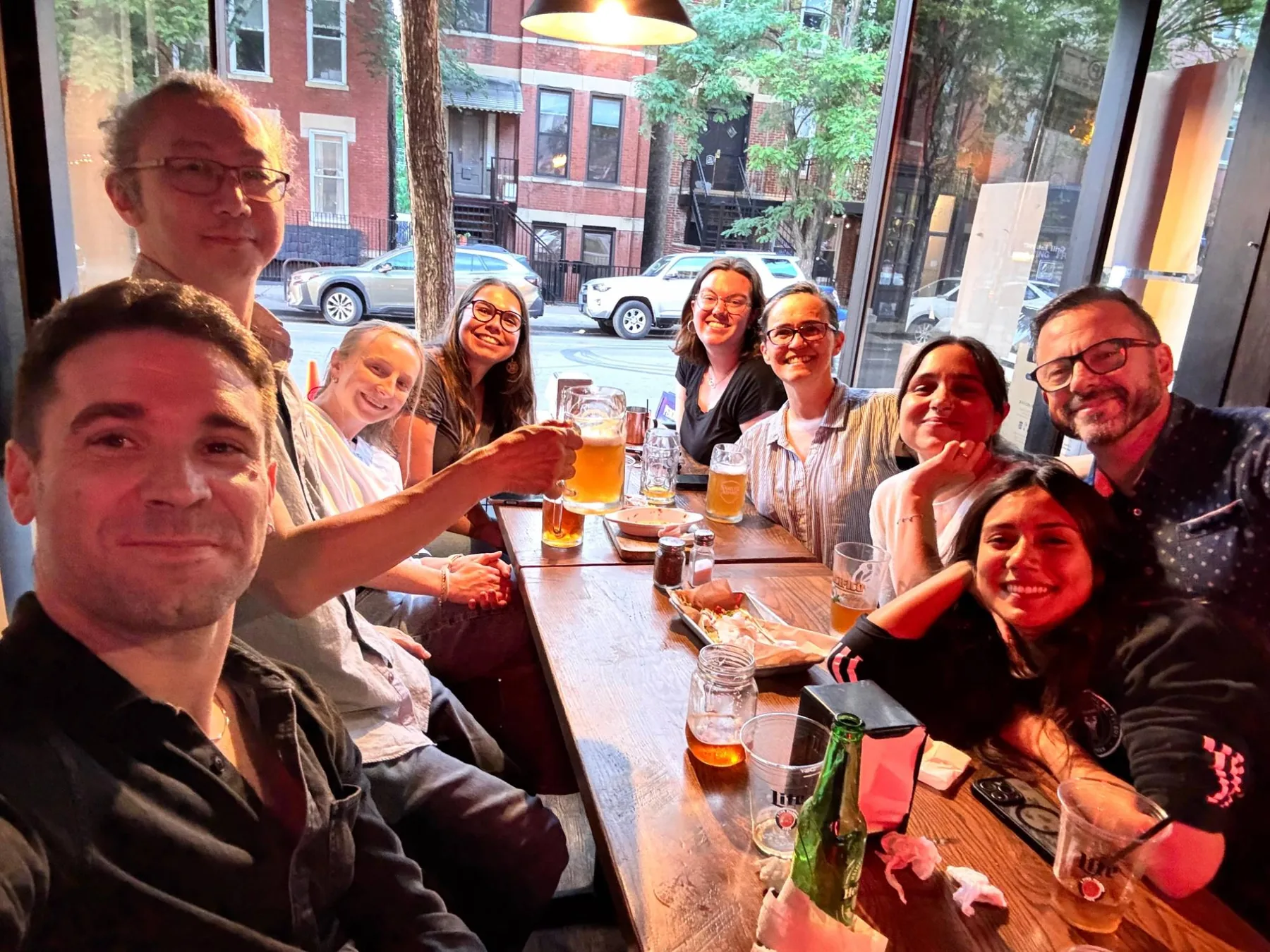 Lab members raising their drinks around a pub table by the window